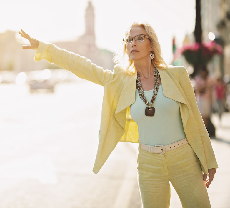 blonde woman in a yellow pantsuit hailing a taxi.